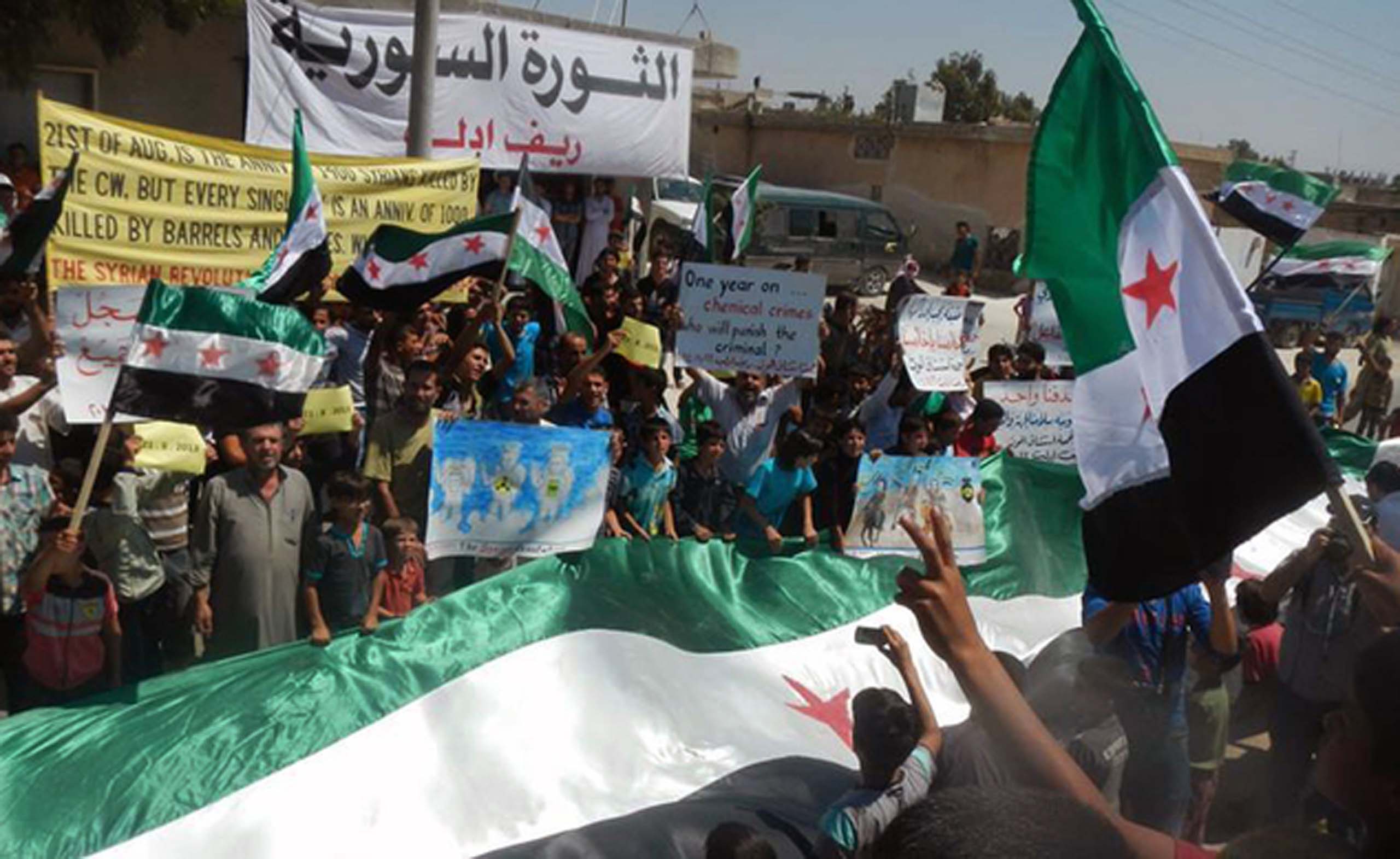 Mideast Syria In this photo provided by an anti-Bashar Assad activist group Edlib News Network (ENN), which has been authenticated based on its contents and other AP reporting, anti-Syrian government protesters carry banners and a giant Syrian revolution flag during a demonstration in Idlib province, northern Syria, Friday, Aug 22, 2014. The death toll from three years of Syria's civil war has risen to more than 191,000 people, the United Nations reported Friday. (AP Photo/Edlib News Network ENN)